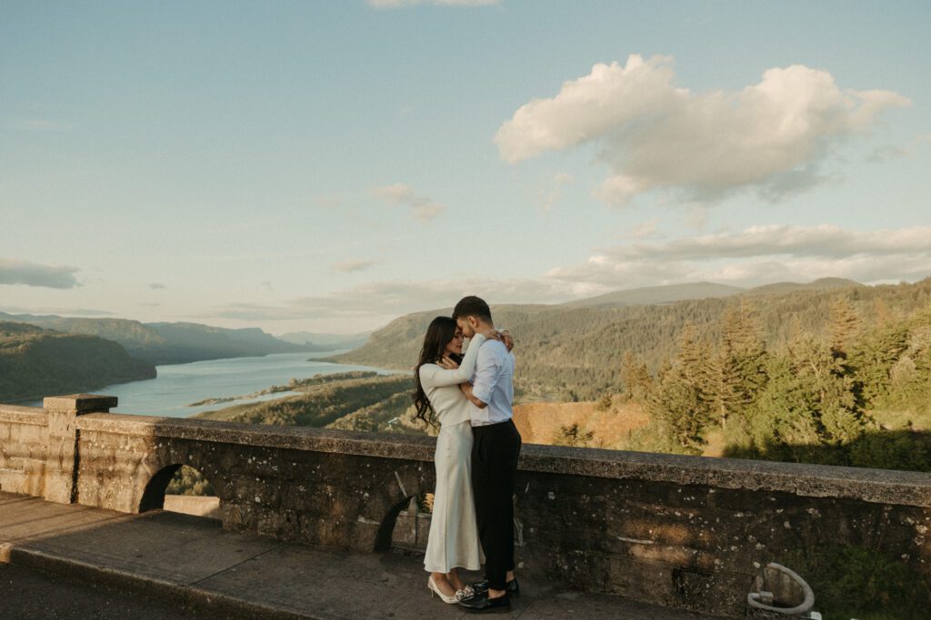 Engaged couple shares a kiss with the view of the Columbia River Gorge from the Vista House behind them