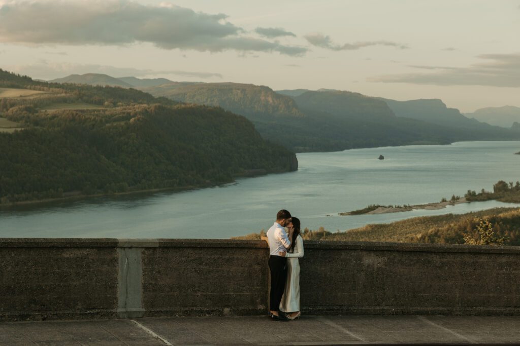 Engaged couple shares a kiss with the view of the Columbia River Gorge from the Vista House behind them