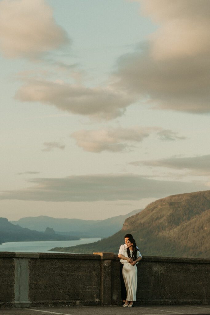 Engaged couple with the view of the Columbia River Gorge from the Vista House behind them