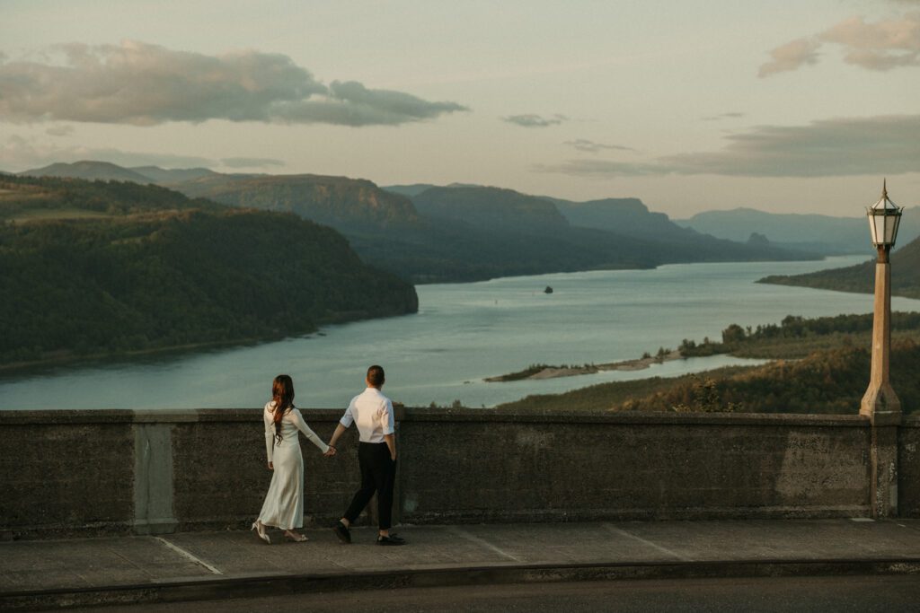 Engaged couple walking hand in hand looking at the view of the Columbia River Gorge from the Vista House